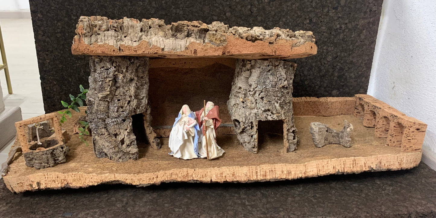 Crèche en liège avec Marie et Joseph portant Jésus, un petit puit se trouve sur le côté