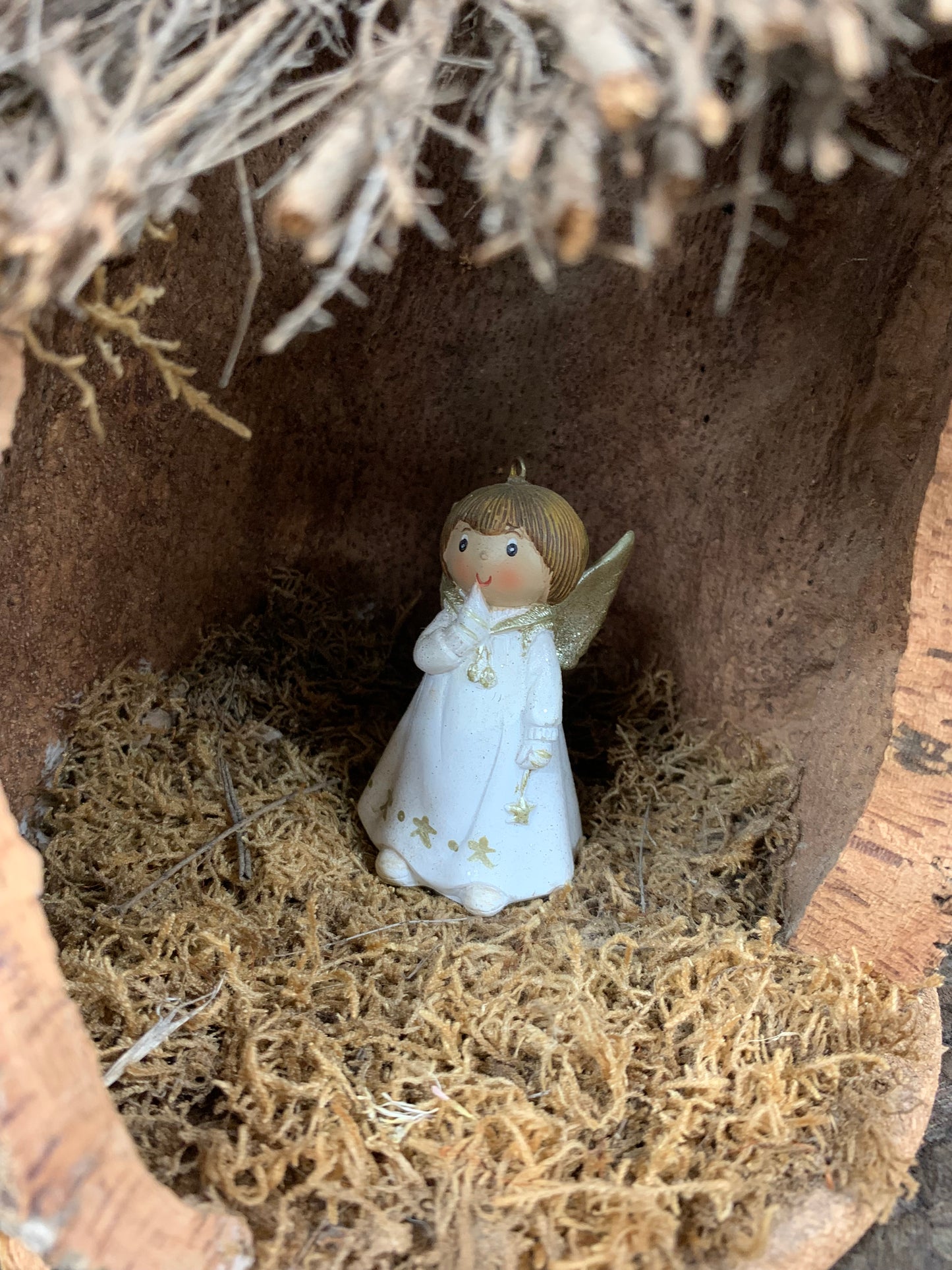 Crèche en liège et en bois, le toit est composé de morceaux de bâtons, de la mousse végétale à l'intérieur avec l'ange posé dessus zoomé sur l'ange